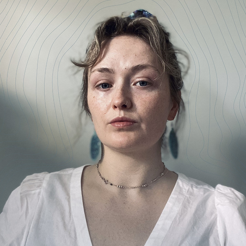 A headshot of a young woman with her hair tied up, dressed in a white shirt and long gemstone earrings