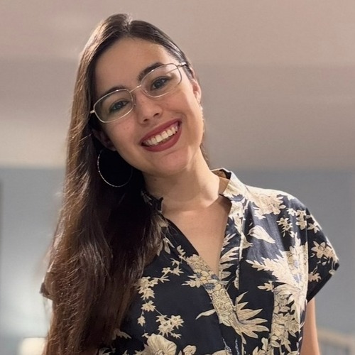 Headshot of a young person with long brown hair and glasses, smiling towards the camera